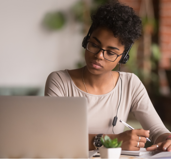 Focused mixed race woman wearing headphones watching webinar write notes